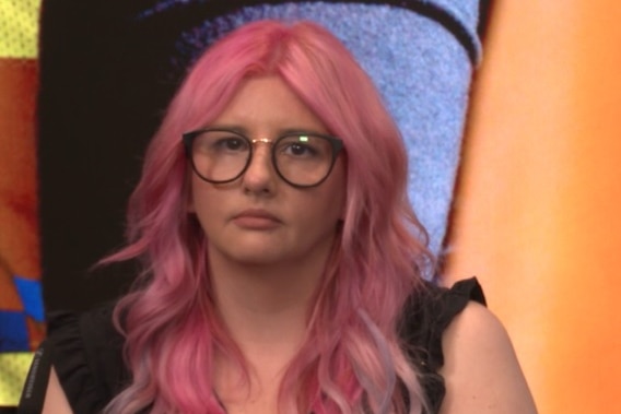Woman with pink hair and glasses looks at camera.