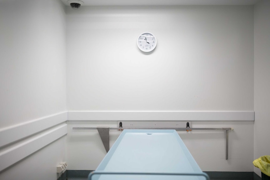 A room including a mortician's slab and a clock.