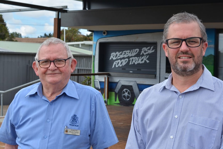 Two men smiling with a food truck behind them.