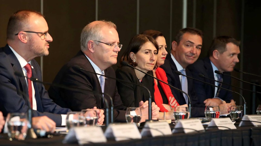 Scott Morrison sits at a panel table. To his left is Gladys Berejiklian, and to his right is Andrew Barr