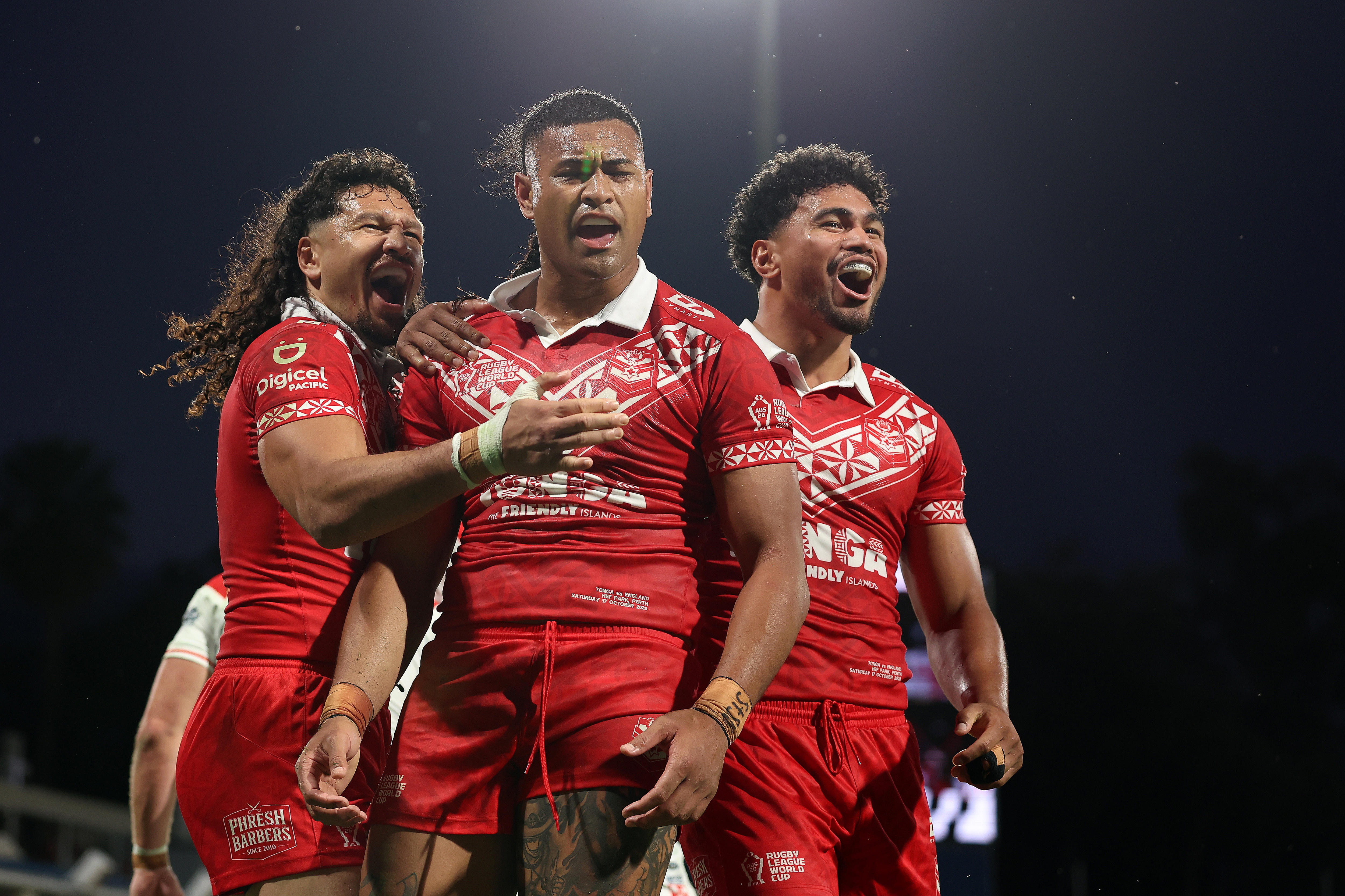 Three rugby league players in red celebrate a try to the camera