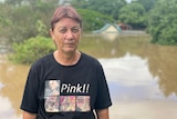 A woman stands in front of flood water. Roof of her house emerged from water in background