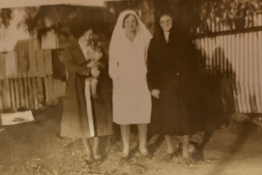 Three women standing in front of a tree with one dressed in nun attire.