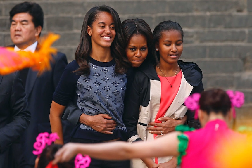 Michelle Obama (C) hugs her daughters Malia (2nd L) and Sasha (R) as they watch a folk dance by performers during her visit at the City Wall, in Xi'an, Shaanxi province