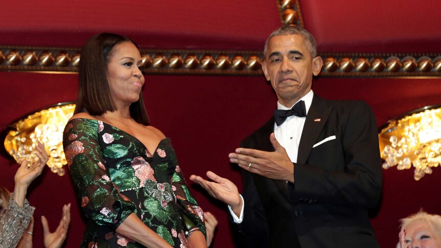 Michelle Obama in an intricate dress stands next to Barack Obama in a tuxedo.