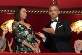 Michelle Obama in an intricate dress stands next to Barack Obama in a tuxedo.