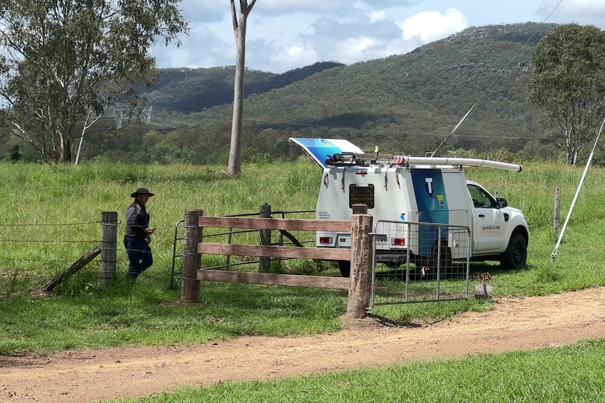 Wide shot of a rural landscape with a Telstra technician's vehicle in the centre and a man walking towards it