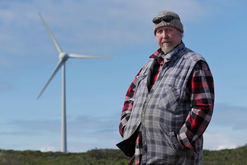 A man stands in front of a wind turbine