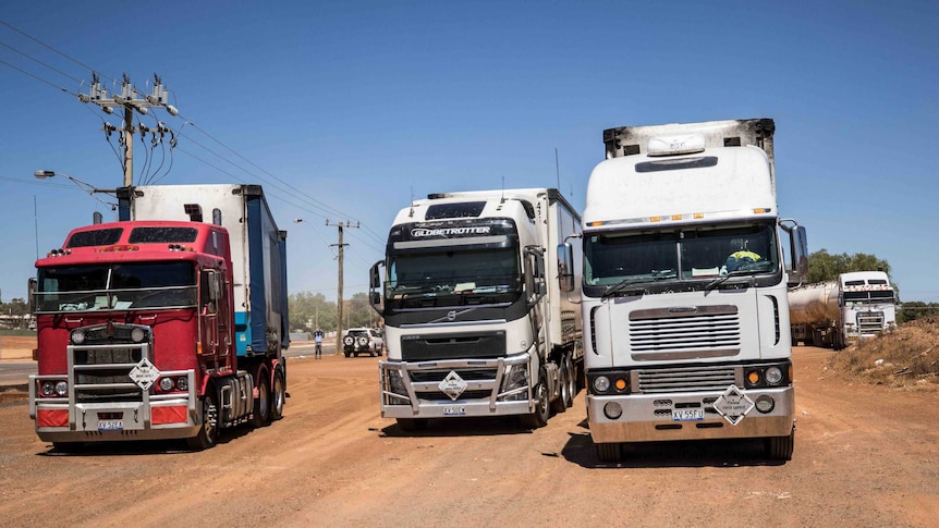 Three trucks parked up on sandy road