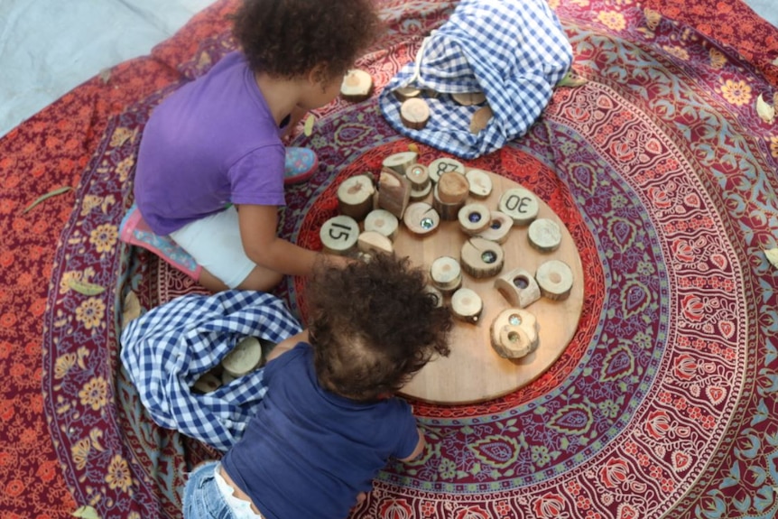 Two little girls play with natural wooden blocks on a colourful mat outside