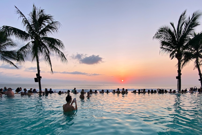 People swimming in a pool facing the ocean during sunset in Seminyak Beach, Bali, Indonesia.