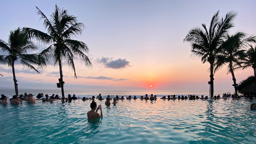 People swimming in a pool facing the ocean during sunset in Seminyak Beach, Bali, Indonesia.