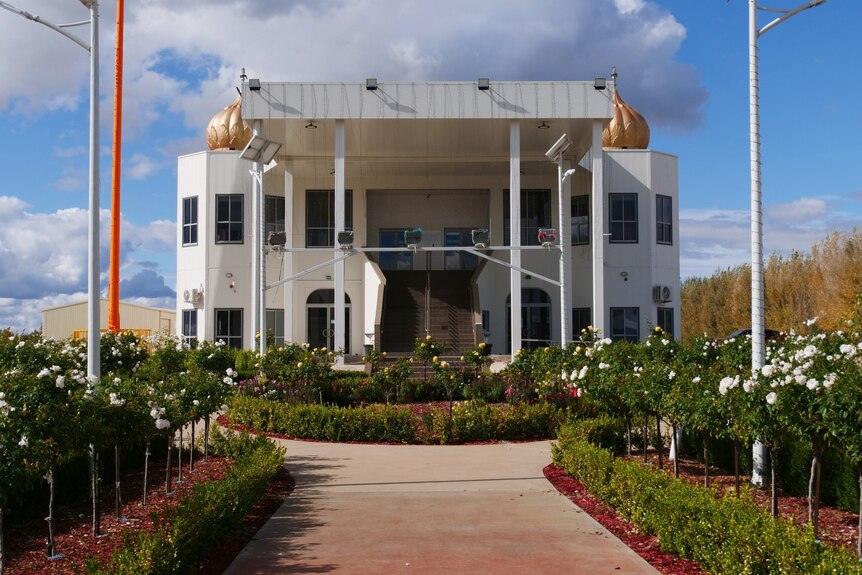 A white Sikh temple with a footpath and garden beds in the foreground leading towards the steps of the temple. 