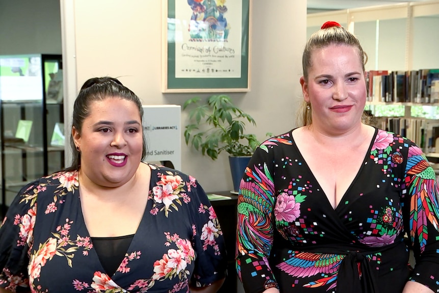 Two women wearing black and floral dresses. 