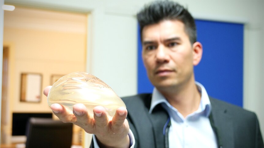 Adrian Sjarif holds a breast implant out and looks at it.
