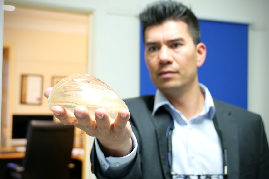 Adrian Sjarif holds a breast implant out and looks at it.