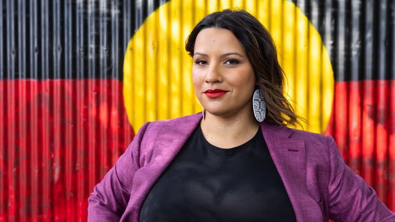 Woman stands proud behind Aboriginal flag