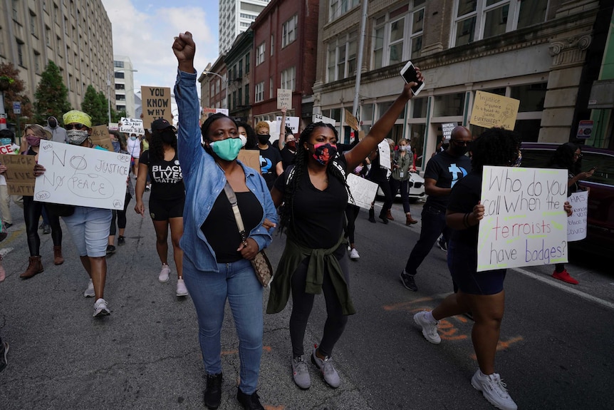 A group of people march with their hands in the air and holding up signs on a street