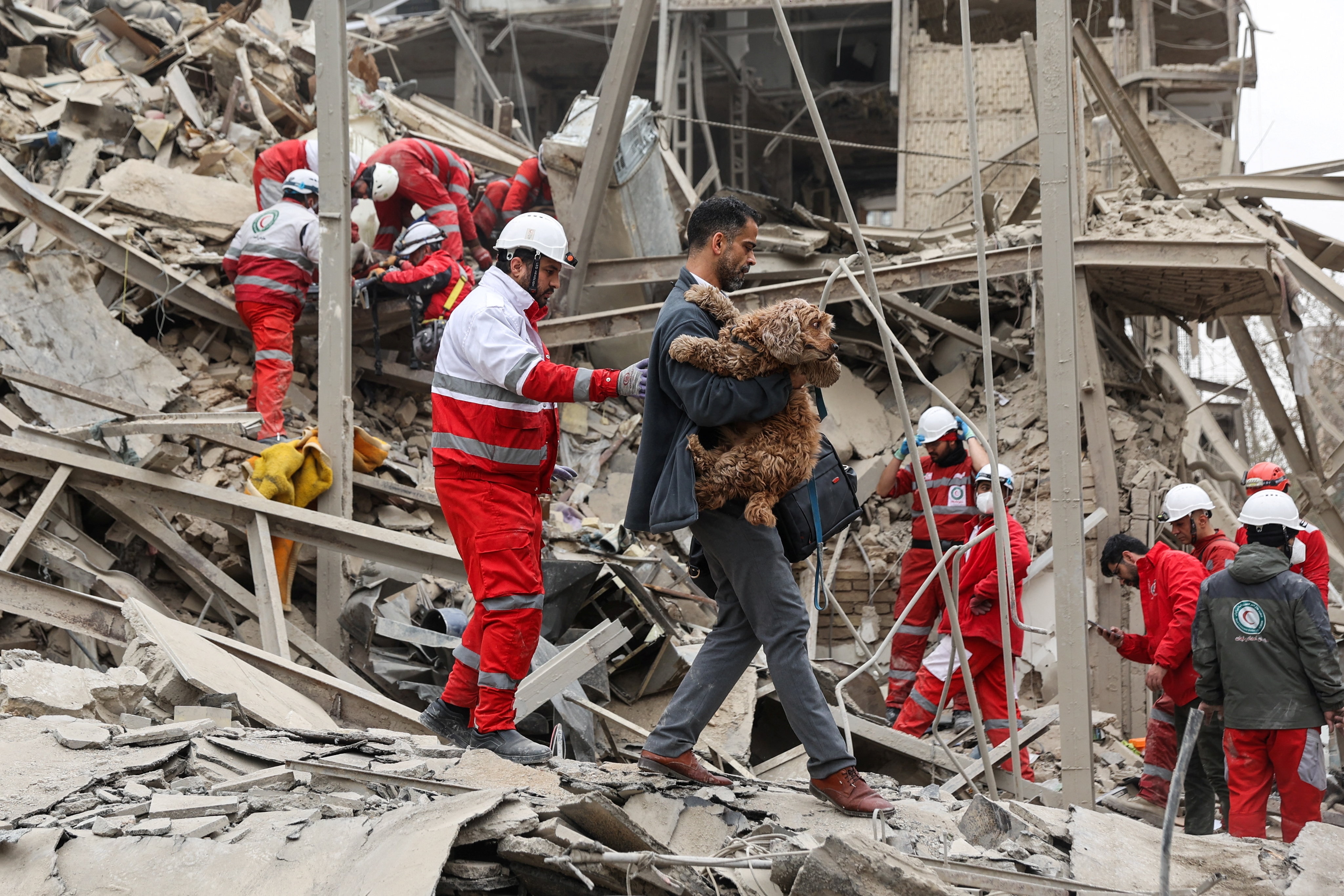 A man carrying his dog out of rubble with emergency workers around him.