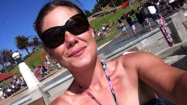 A woman with brown hair tied back and big sunglasses takes a selfie in a park on a sunny day.