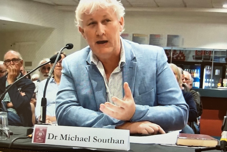 man seated at table in front of microphone 