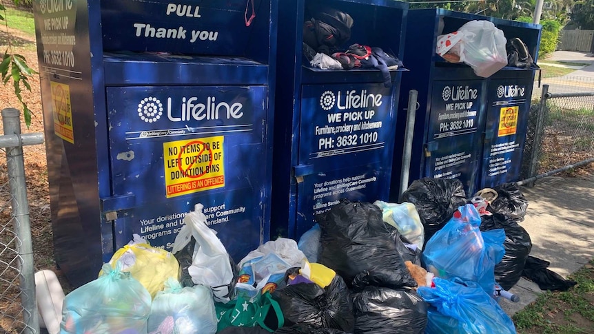 Four charity bins from Lifeline overflowing with donations and items strewn in front of them.