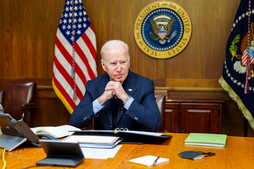 President Joe Biden rests his hands under his chin while sitting at a desk at Camp David.