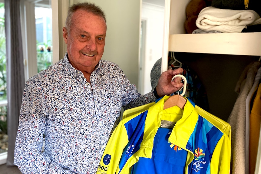 A grey-haired smiling man holding a Sydney 2000 Olympics volunteer shirt.