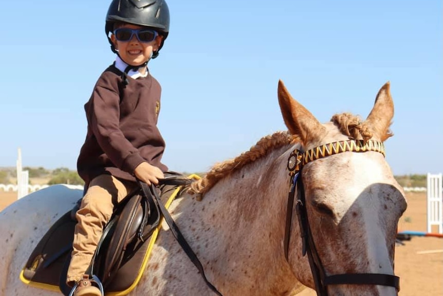 A small child sits on top of a white horse smiling. 