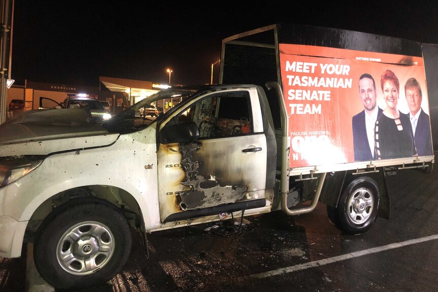 A burnt car with a billboard.