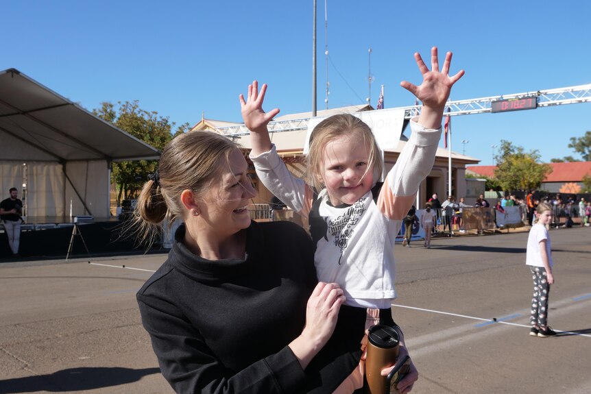a woman holds a young girl, who has her arms up in the air in celebration