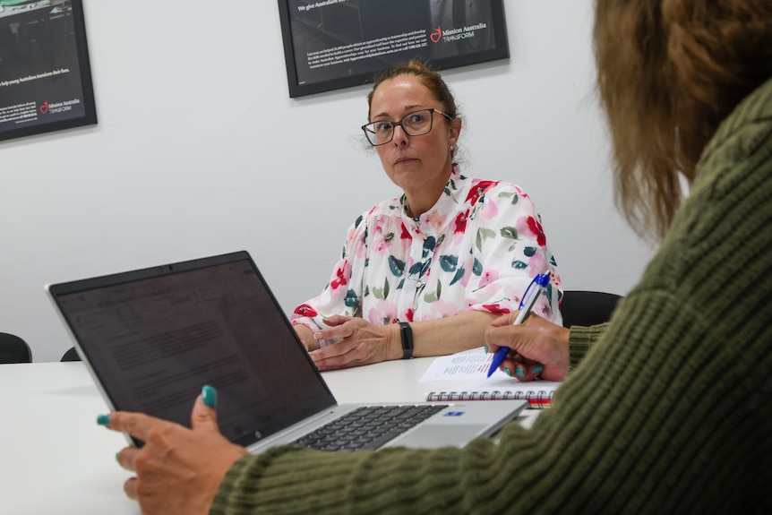 A woman wearing a brightly patterned shirt looks over a laptop.