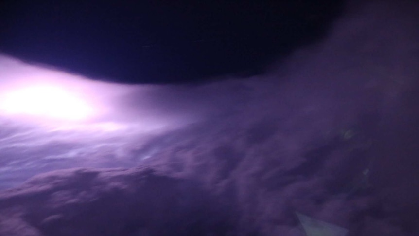 A dark night sky can be seen in the middle of a round sea of cloud. The night has given the clouds a purple hue.