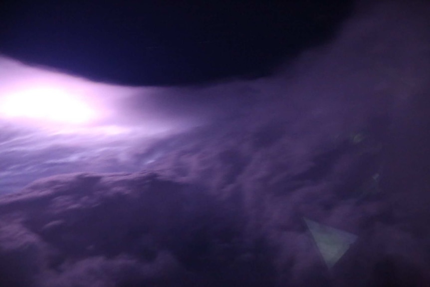 A dark night sky can be seen in the middle of a round sea of cloud. The night has given the clouds a purple hue.