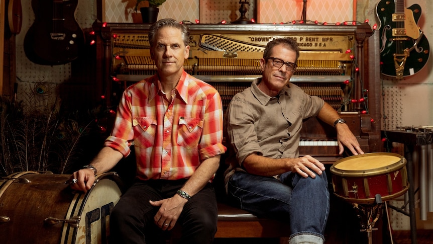 Calexico's Joey Burns and John Convertino pose in a studio in front of an open piano