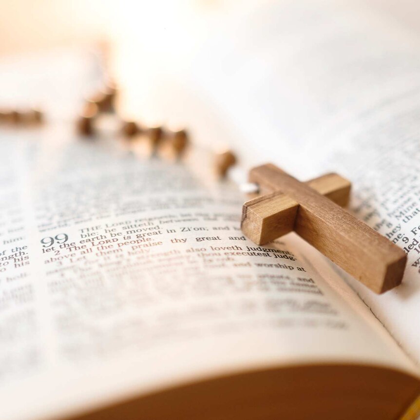 wooden rosary cross lying on top of open bible pages