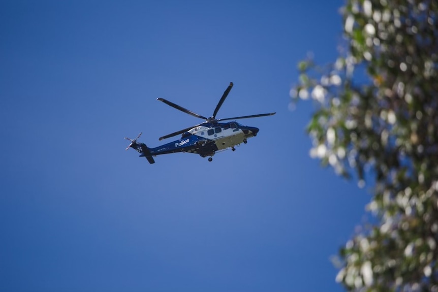 A search helicopter is seen in the air against a clear blue sky. 