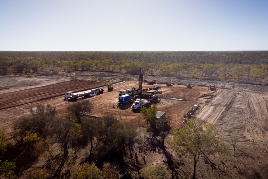 An aerial view of several lines of trucks parked on a large, cleared patch of dirt, surrounded by scrub.