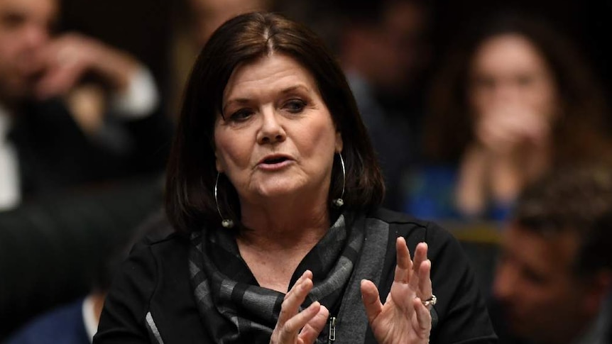 A woman with dark hair gestures as she speaks.