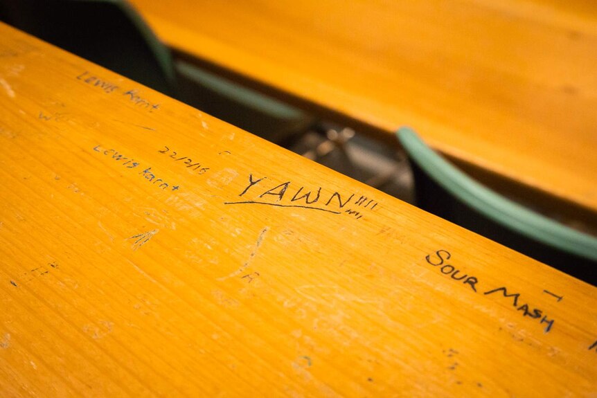 Student graffiti covers desks at the back of a lecture theatre.