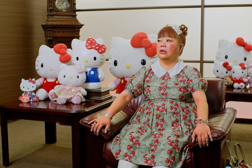 A woman sits in front of a table full of Hello Kitty dolls