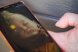 A close up photo of Tamika holding her mobile phone with a photo of her baby daughter sleeping as the screensaver.