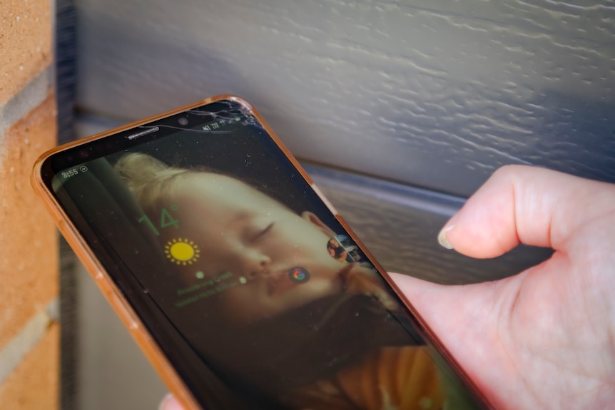 A close up photo of Tamika holding her mobile phone with a photo of her baby daughter sleeping as the screensaver.