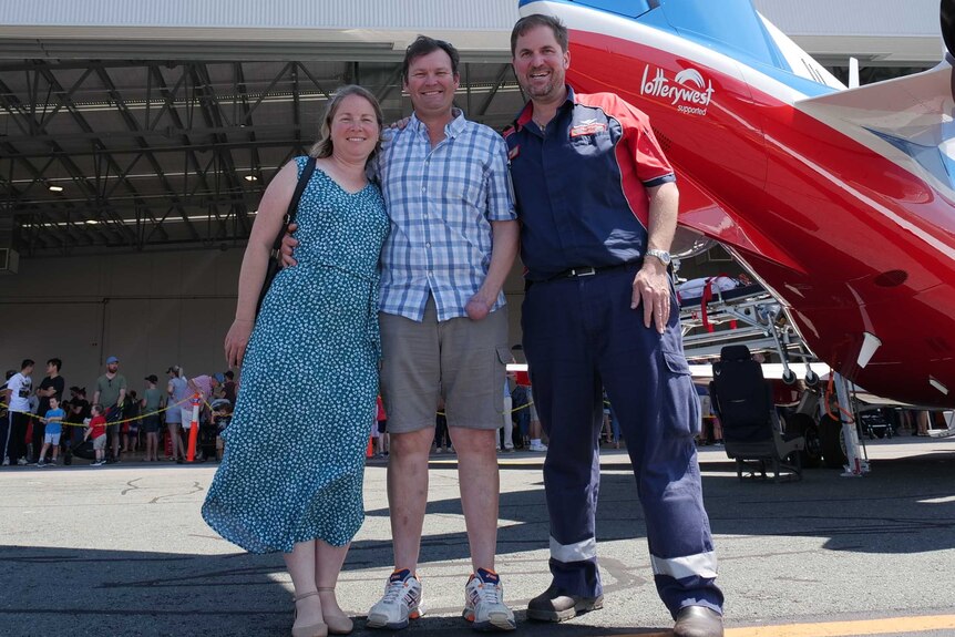 A woman and two men stand smiling next to a red and blue RFDS plane.