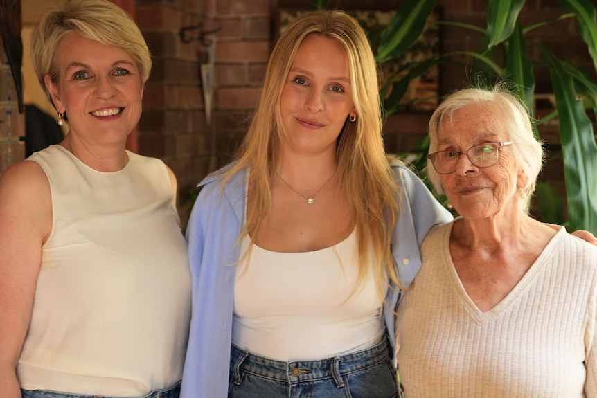 Three women of three generations stand smiling 