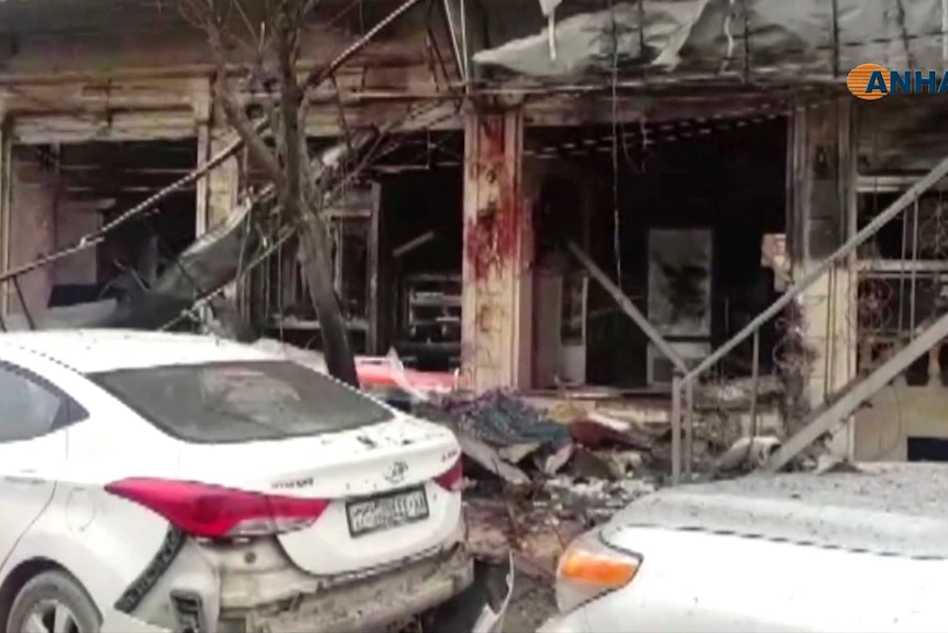 A shop front lays in pieces with debris strewn all over the area and blood smears on the walls.