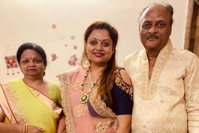 A woman wearing a pink sari stands in the middle of an older woman wearing a yellow sari and a man.