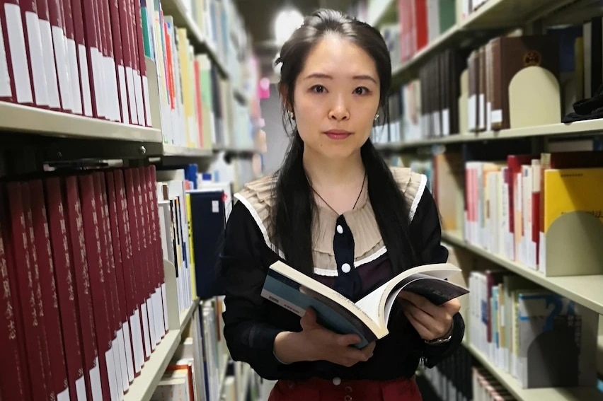 A Chinese female scholar is holding a book in the library 