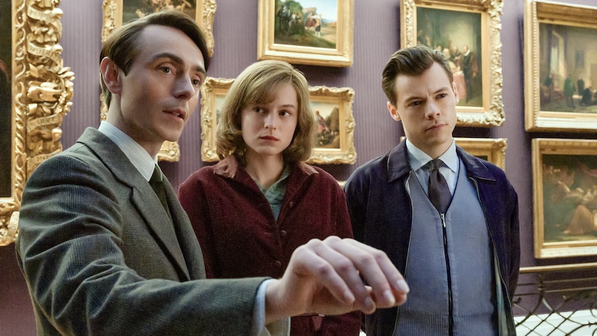 David points at art out of the frame as Emma looks at him and Harry stares ahead, all in character in a museum.