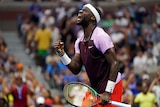 A headband-wearing tennis player closes his eyes, pumps his fist and shouts in celebration during a match.